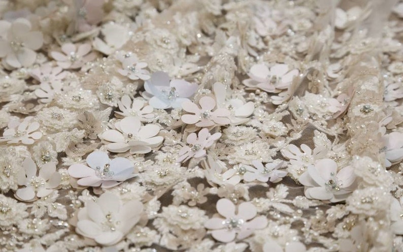 May include: White fabric with a delicate floral pattern. The fabric is covered in small, white flowers with a raised texture. The flowers are arranged in a random pattern and are interspersed with small, white beads.