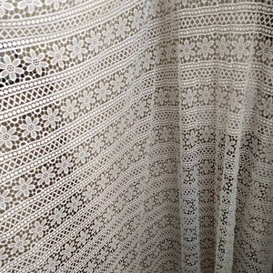 May include: White crochet fabric with a floral pattern. The fabric has a delicate, lacy texture and is perfect for crafting or sewing projects.