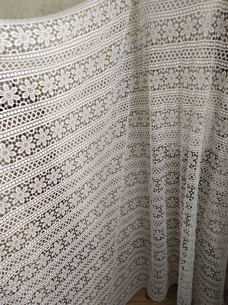 May include: White crochet fabric with a floral pattern. The fabric has a delicate, lacy texture and is perfect for crafting or sewing projects.