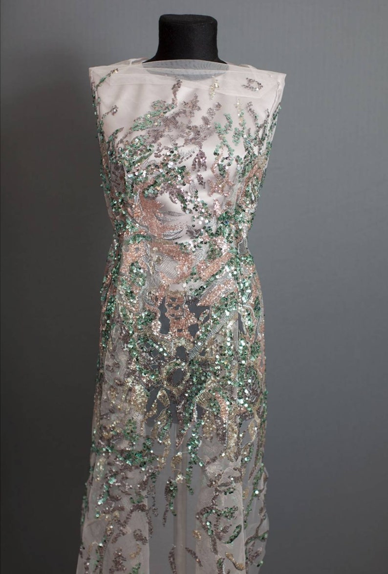 May include: A sheer fabric with a green, gold, and pink sequined design. The fabric is draped over a dress form.