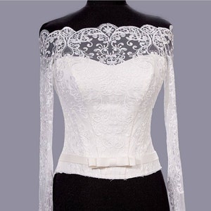 Puede incluir: Corsé de vestido de novia blanco de encaje con hombros descubiertos, mangas largas y cintura ajustada. El corsé tiene un delicado patrón de encaje floral y una cinta de satén con un lazo en la cintura.