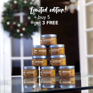 May include: A stack of eight gold and silver jars of body polish with the text "ABUNDANCE holiday body polish" on the front. The jars are arranged in a pyramid shape. The text "Limited edition! + buy 5 get 3 FREE" is written above the jars.