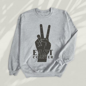 May include: A grey sweatshirt with a black peace sign and the text "East Coaster" printed on the front.