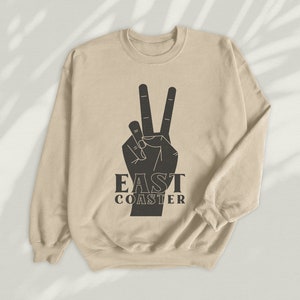 May include: A beige sweatshirt with a black peace sign and the text "East Coaster" printed on the front.