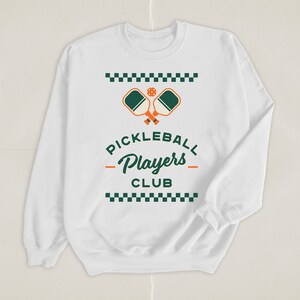 May include: White long-sleeve sweatshirt with a green and orange pickleball paddle graphic and the text "Pickleball Players Club" in green and black.