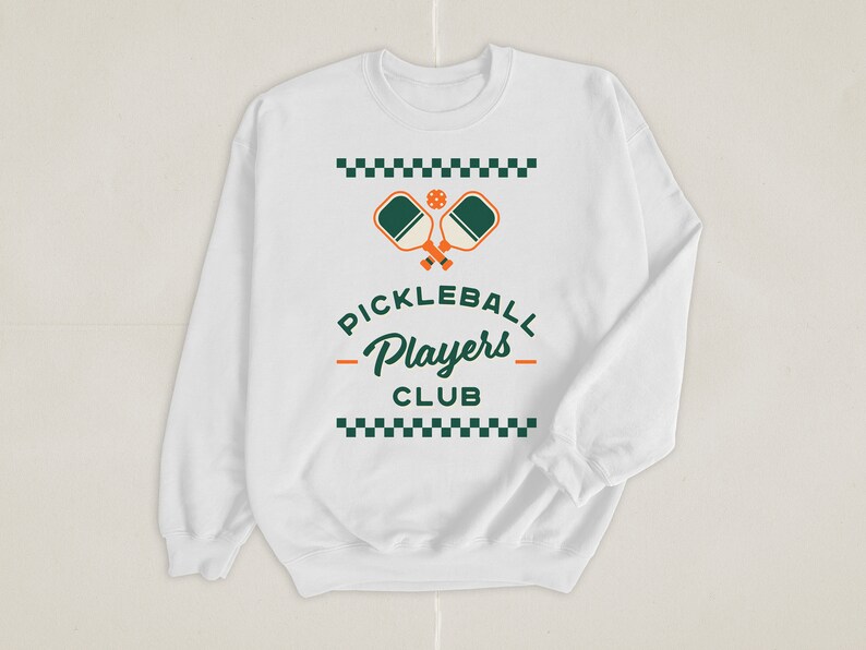May include: White long-sleeve sweatshirt with a green and orange pickleball paddle graphic and the text "Pickleball Players Club" in green and black.
