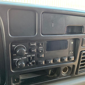 May include: Close-up of a black car dashboard with a radio and climate control panel. The radio has buttons for AM/FM, seek, set, and volume. The climate control panel has buttons for fade, tune, and bass treble. The dashboard also has a small storage compartment and a vent.