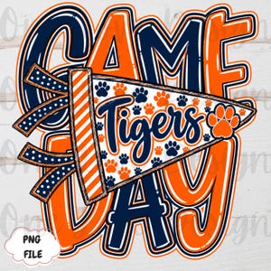 May include: A graphic design featuring the text GAME DAY in large orange and navy blue letters. A pennant flag is layered over the text, displaying the word Tigers in navy blue script, surrounded by orange and navy blue paw print patterns.