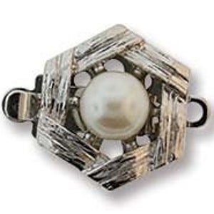 Könnte beinhalten: Ein silberfarbener Schmuckverschluss mit sechseckigem Design. Der Verschluss hat ein strukturiertes, gewebtes Muster um eine zentrale, runde, weiße Perle. Der Verschluss hat zwei kleine Schlaufen auf beiden Seiten zur Befestigung.