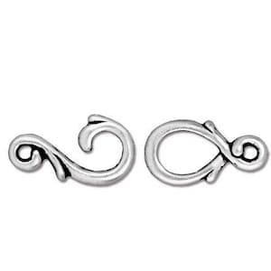 May include: Silver-toned metal clasp with a decorative, ornate design. The clasp is made of two pieces, one with a loop and the other with a hook.