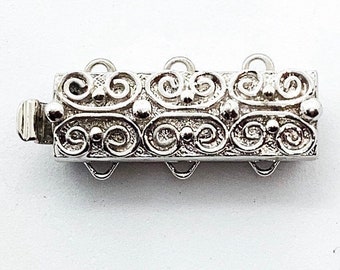 May include: Silver-toned metal extender chain with a decorative, ornate design. The chain has four loops for attaching to a necklace or bracelet.