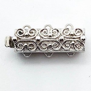 May include: Silver-toned metal extender chain with a decorative, ornate design. The chain has four loops for attaching to a necklace or bracelet.