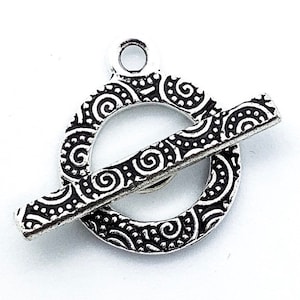 Peut inclure: Fermoir à bascule en métal argenté avec un motif décoratif en spirale. Le fermoir a un anneau rond et une barre qui coulisse à travers l'anneau.