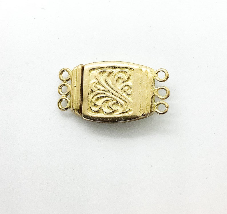 May include: Gold-toned metal clasp with a decorative floral design and three loops. The clasp is designed to connect two strands of jewelry.
