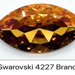 Peut inclure: Gros plan sur un seul cristal Swarovski de forme marquise, facett&eacute;, de couleur ambre. Le cristal est &eacute;tiquet&eacute; "Swarovski 4227 Brandy".