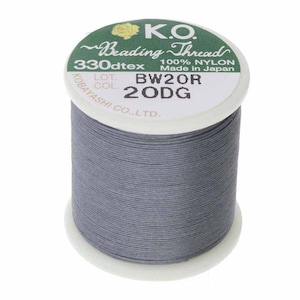 Pode incluir: Um carretel de fio cinza K.O. Beading Thread, 100% nylon, 330dtex, fabricado no Japão. O rótulo inclui o número do lote BW20R e o código de cor 20DG. O fio é enrolado em um carretel branco.