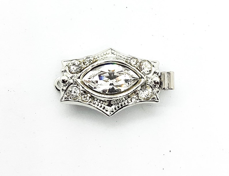 May include: Silver-toned clasp with a clear marquise-shaped crystal surrounded by smaller clear crystals.