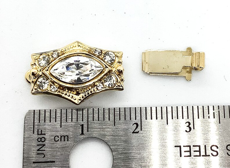 May include: Gold-tone clasp with a large clear marquise-shaped rhinestone surrounded by smaller rhinestones. The clasp measures approximately 1 inch in length.