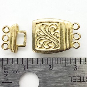 May include: Gold-tone metal clasp with a decorative floral design. The clasp measures approximately 2 cm in length.