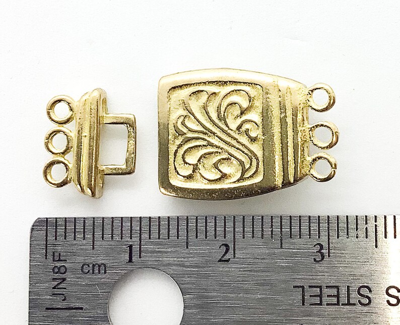 May include: Gold-tone metal clasp with a decorative floral design. The clasp measures approximately 2 cm in length.