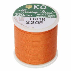 Pode incluir: Um carretel de fio para miçangas laranja K.O., 100% nylon, 330dtex. O rótulo diz "Made in Japan" e inclui os códigos TTO1R e 220R. O carretel está em uma base branca.