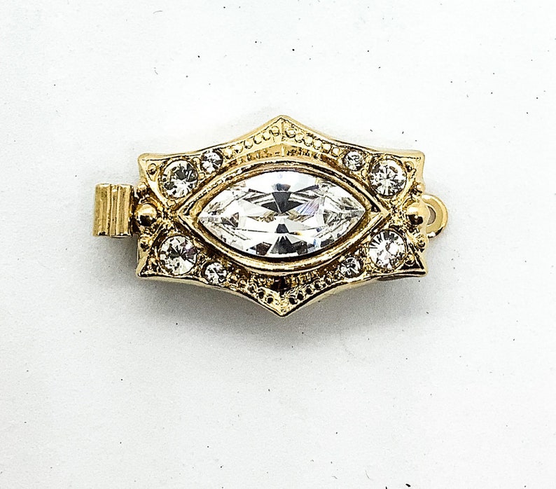May include: Gold-toned clasp with a large clear marquise-shaped crystal surrounded by smaller clear crystals.
