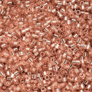 May include: A close-up of a pile of small, cylindrical beads in a soft, rose-gold colour. The beads have a metallic sheen and are densely packed together, creating a textured surface. These beads are suitable for jewellery making and crafts.