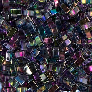 Peut inclure: Gros plan sur un tas de perles rectangulaires iridescentes. Les perles sont un mélange de couleurs, dont le violet, le vert et l'or, avec un éclat métallique. Chaque perle a deux trous pour l'enfilage. Les perles sont éparpillées, créant une surface texturée.