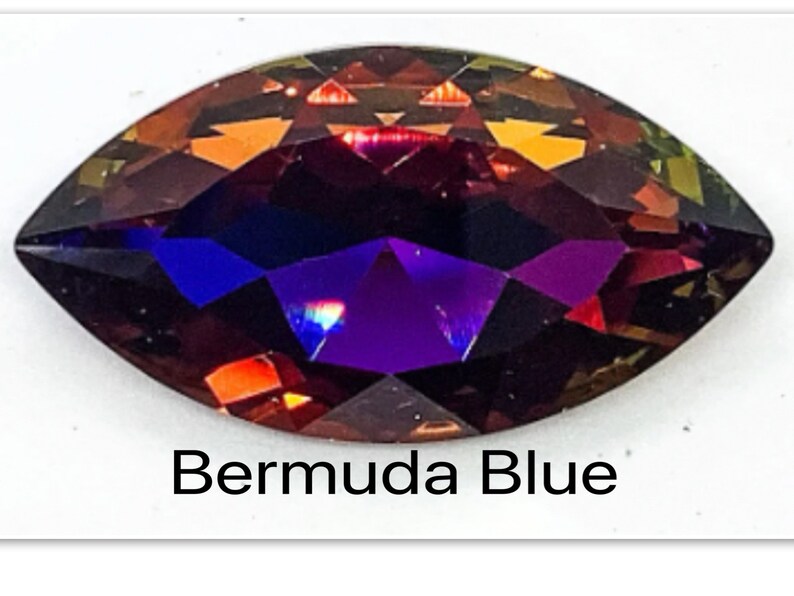 Peut inclure: Gros plan sur une pierre pr&eacute;cieuse facet&eacute;e et iris&eacute;e de forme marquise. La pierre pr&eacute;cieuse a une teinte violette fonc&eacute;e avec des nuances de rouge et d'orange. Le texte "Bermuda Blue" est &eacute;crit sous la pierre pr&eacute;cieuse.