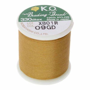 Pode incluir: Um carretel de fio para miçangas K.O. na cor amarelo dourado. O rótulo diz "100% NYLON" e "Made in Japan". O carretel tem uma base branca e um rótulo verde e branco com o texto "330dtex" e "XBO1R 09GD."
