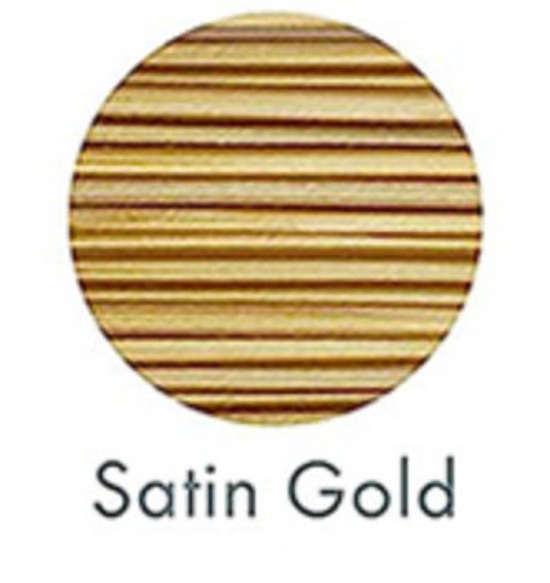 May include: A circular, gold-colored object with horizontal lines, labeled "Satin Gold" in a handwritten font. The object appears to be made of wood or a similar material, with a satin finish.