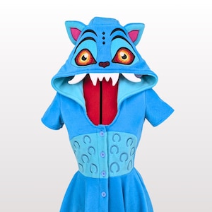 May include: A blue hooded dress with a cat-like design. The hood features cat ears, large orange eyes, and white fangs. The dress has a button-down front, a fitted waist with crescent moon details, and a flared skirt with a black hem.