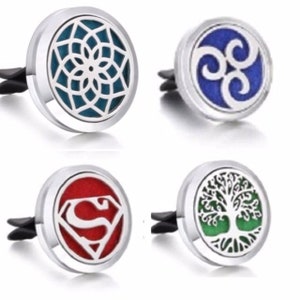 May include: Four silver car air fresheners with different designs. The first is a blue and white mandala, the second is a blue and white triquetra, the third is a red and white Superman logo, and the fourth is a green and white tree of life.