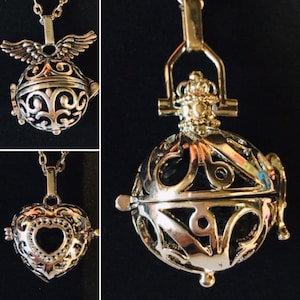 May include: Three silver charm necklaces with intricate designs. The charms are in the shape of a heart, a circle with wings, and a circle with a crown. The necklaces are all on a black background.