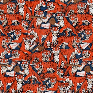 May include: A repeating pattern fabric featuring orange and black tigers playing baseball on a dark blue background. The tigers are depicted with baseball bats, gloves, and pennants with the word Detroit printed in white on a red background.