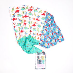 May include: Three fabric panels with different patterns. The first panel has a white background with a repeating pattern of colorful dinosaurs. The second panel has a turquoise background with a repeating pattern of eyeglasses. The third panel has a blue background with a repeating pattern of colorful speech bubbles with the words "POW", "BANG", and "ZOOM".