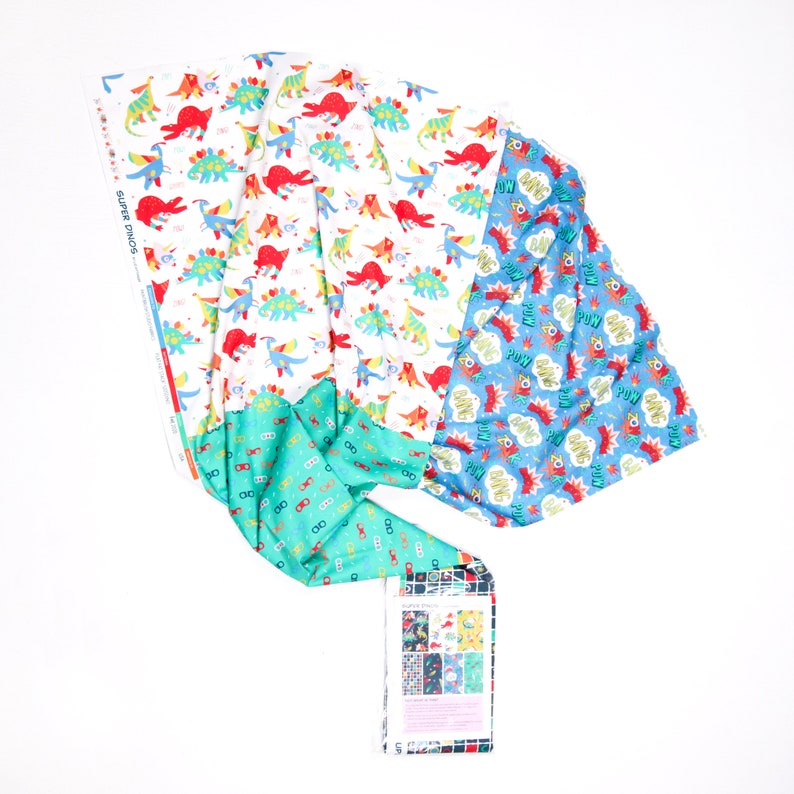 May include: Three fabric panels with different patterns. The first panel has a white background with a repeating pattern of colorful dinosaurs. The second panel has a turquoise background with a repeating pattern of eyeglasses. The third panel has a blue background with a repeating pattern of colorful speech bubbles with the words "POW", "BANG", and "ZOOM".