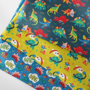 May include: Three fabric swatches with different patterns. The top swatch is dark blue with a repeating pattern of colorful dinosaurs and the words "ZOMP", "WHOMP", and "ZING". The middle swatch is yellow with a repeating pattern of colorful dinosaurs and the words "BANG" and "ZONK". The bottom swatch is blue with a repeating pattern of colorful explosions and the words "BANG", "ZONK", and "POW".
