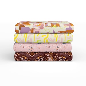 May include: Four fabric swatches stacked on top of each other. The top swatch has a light beige background with a pattern of brown and purple buildings. The second swatch has a light beige background with a pattern of yellow and pink abstract shapes. The third swatch has a light pink background with a pattern of small white flowers and blue and yellow geometric shapes. The bottom swatch has a dark brown background with a pattern of small white flowers and brown leaves.