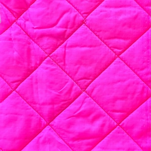Peut inclure: Gros plan sur un tissu matelassé rose vif. Le tissu est cousu selon un motif en losanges, créant une surface texturée. La couleur est un rose vif et saturé, avec de légères variations de ton dues au matelassage.