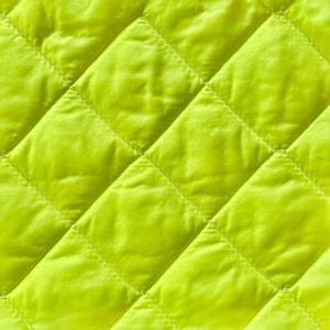 May include: Close-up of a bright yellow quilted fabric. The fabric features a diamond pattern created by stitched lines. The material appears smooth and slightly shiny, with subtle texture within each diamond.