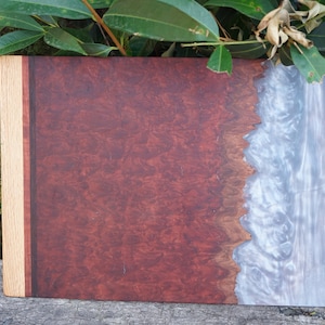 May include: A rectangular wooden cutting board with a dark red wood grain on one side and a white and gray epoxy resin on the other side. The board has a light brown wood border.