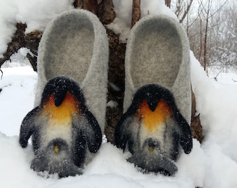 Op de afbeelding: Een paar grijze wollen pantoffels met pinguïnontwerpen. De pinguïns hebben zwart-witte veren, oranje snavels en gele borsten.