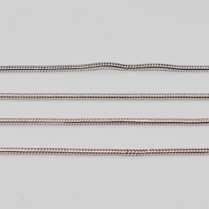 May include: Close-up of four silver-colored snake chains. The chains are displayed against a white background. The chains have a smooth, flexible design, with a tightly woven pattern. The top chain has a slight bend in the middle.