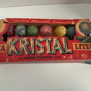May include: A box of vintage Christmas lights with the brand name "Kristal Lites" and the text "Sparkling Illuminated Ornaments with General Electric Lamps". The box contains a string of multi-coloured, sparkly, round Christmas lights.