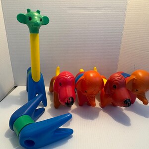 Può includere: Un set di giocattoli in plastica colorati raffiguranti animali, tra cui una giraffa e tre elefanti. La giraffa ha la testa verde, il collo giallo e il corpo blu. Gli elefanti sono rossi e arancioni con dettagli blu e gialli.