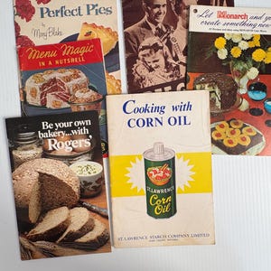 以下が含まれることがあります： 「Perfect Pies」や「Cooking with Corn Oil」などのタイトルを含む、ヴィンテージの料理本のコレクション。表紙には焼き菓子のイラストやレトロなグラフィックが描かれています。