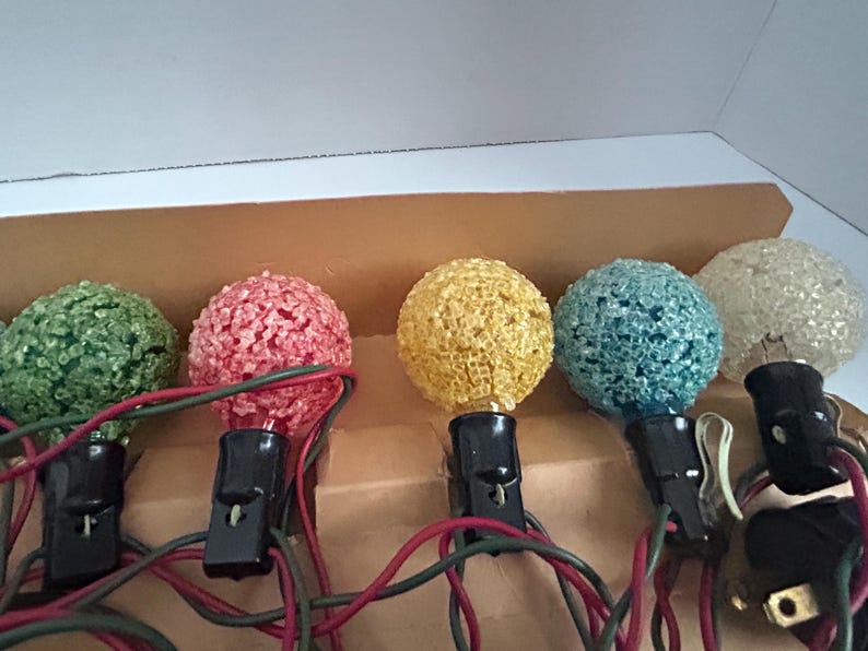 May include: A set of six vintage Christmas lights with textured bulbs in green, red, yellow, blue, and white. The lights are wired together and have a plug on the end.