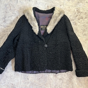 May include: A black faux fur jacket with a white fur collar. The jacket has a single button closure and a label that reads "Elizabeth Fashions".