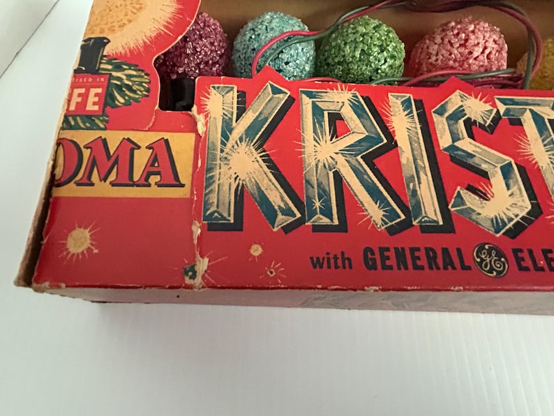May include: Vintage box of Christmas lights with a red background and the text "KRISTMAS" in large, glittery letters. The box also features the text "with GENERAL ELECTRIC" and the General Electric logo.